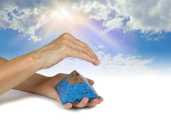 Sensing Orgone Pyramid Resonance on Cobalt Blue Silk background - Female holding an orgone pyramid in left hand with right hand hovering above sensing energy against blue sky background with copy space