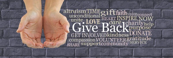 Make a Difference and Give Back Word Cloud - female hands gently cupped beside a GIVE BACK word cloud against a wide grey brick wall background