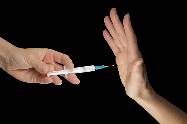 Thanks but I don\'t want your vaccine - hand holding a vaccine syringe opposite a hand in NO position against black background with copy space