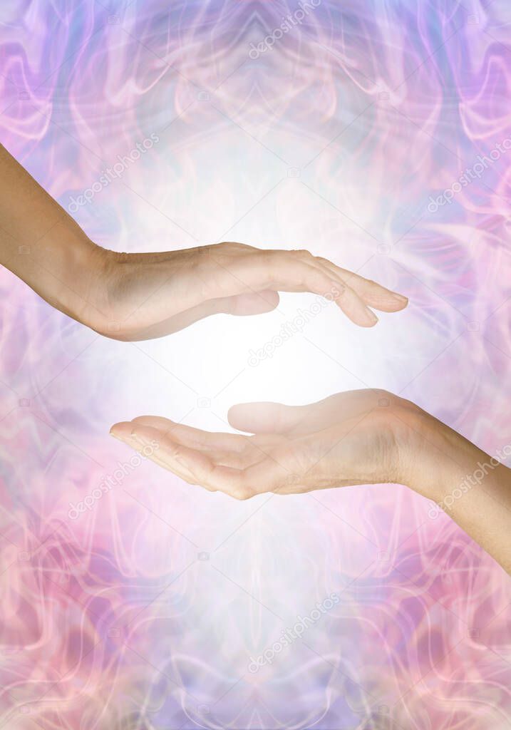 Sensing healing energy coming from palm chakra - female open hand hovering over another open hand with white light between against an ethereal blue lilac pink energy field background with space for text 