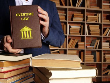 Attorney holds OVERTIME LAW book. Overtime laws require employers to pay employees a wage rate that is greater than their regular rate for hours worked beyond clipart