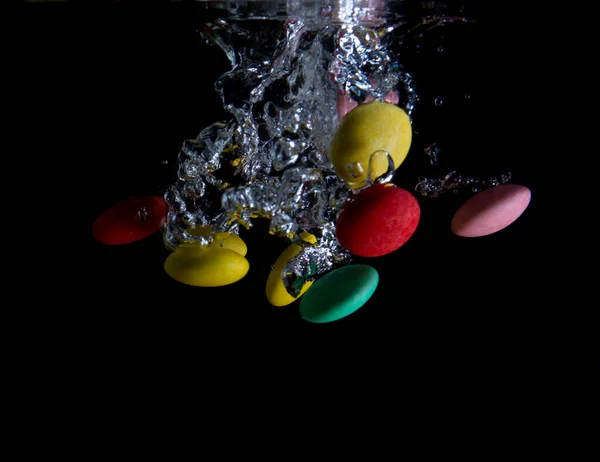 黒を背景に水に飛び散る多色のキャンディー — ストック写真