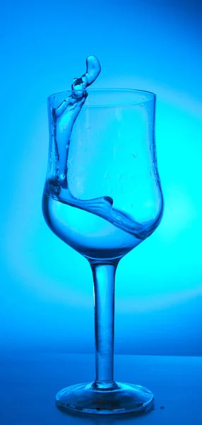 Plons Water Een Glas Een Blauwe Achtergrond — Stockfoto