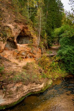 Ligatne, Letonya 'daki mağara kayaları. Güzel ve manzaralı kumtaşı, bulutlu bir sonbahar gününde Ligatne nehrinin kenarındaki mahzen mağaraları ile birleşir.