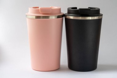 Beyaz arka planda çay ya da kahve için iki termo bardak ya da termos bardağı. Adam ve kadın için siyah ve pembe. Çiftler için sıcak içecek