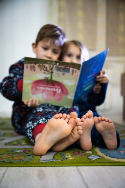 Erkek ve kız kardeşler pijamalarıyla kitap okurlar.