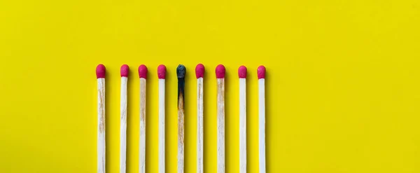 Success, defeat, achievement. The concept of happiness. Matches on yellow background. Burnt dark match among normal matches. Burning match fire to its neighbors, a metaphor for ideas and inspiration