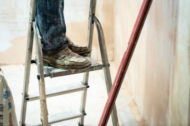 Duvar sıvama aletleriyle ev yenileme yapan bir el işçisi. Kapalı duvarları ve tavanları alçı ve şamandıra ile yenileyen sıva. Odaya el yapımı spatulayla duvar ören mutlu işçi.