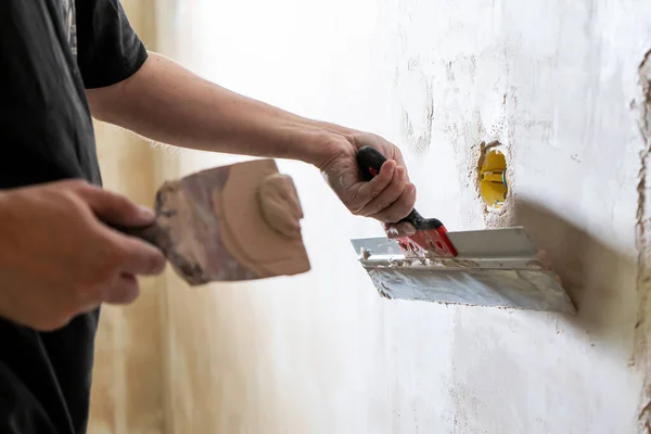 Manual worker with wall plastering tools renovating house. Plasterer renovating indoor walls and ceilings with float and plaster. Happy worker man making wall in the room by hand spatula