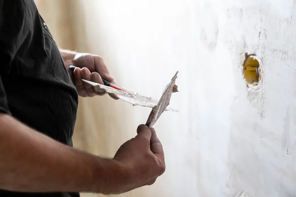 Manual worker with wall plastering tools renovating house. Plasterer renovating indoor walls and ceilings with float and plaster. Happy worker man making wall in the room by hand spatula