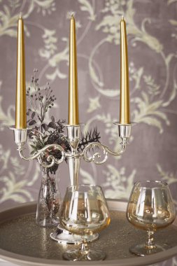 Eski tarz retro mumlar ve bir tepside şarap kadehi, bir masada klasik ev dekorasyonu, açık tonlarda.