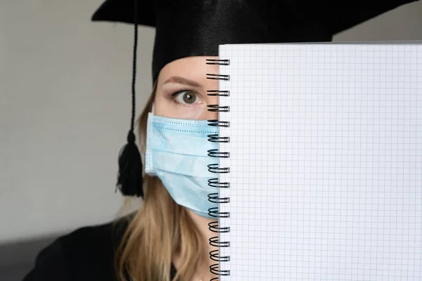A student in mask is wearing a graduation cape and robe holding blank copy space place concept of the class 2021 coronavirus pandemic of the covid. Graduation student on white background