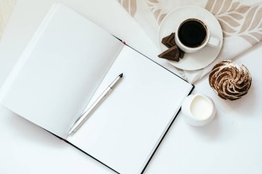 Bir fincan sade kahve, çikolatalı kek ve açık not defteri.