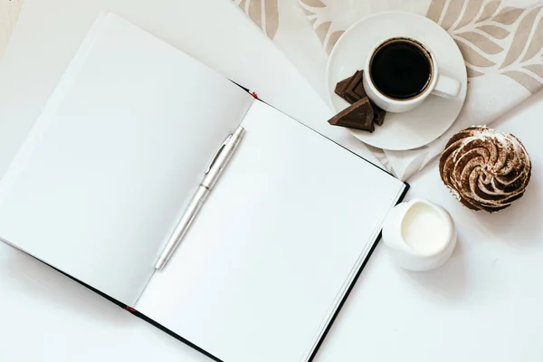 Bir fincan sade kahve, çikolatalı kek ve açık not defteri.