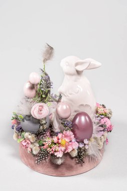 Paskalya masa kompozisyonu tavşanlar ve Paskalya yumurtaları, beyaz arka planda nergis sarısı çiçekler beyaz örülmüş kaplarda. Çiçekli Paskalya tavşanı
