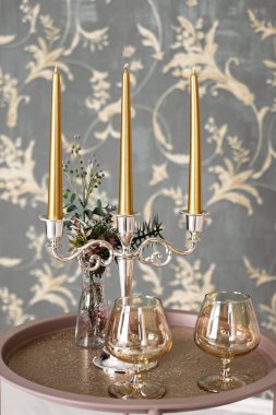 Eski tarz retro mumlar ve bir tepside şarap kadehi, bir masada klasik ev dekorasyonu, açık tonlarda.