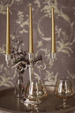 Eski tarz retro mumlar ve bir tepside şarap kadehi, bir masada klasik ev dekorasyonu, açık tonlarda.