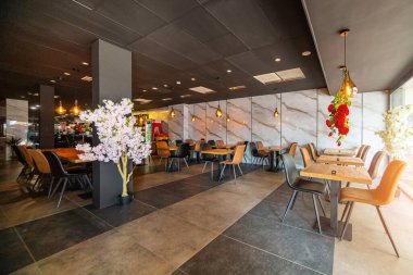 Modern ve zarif bir yemek alanı sunan güzel tasarlanmış bir restoran iç mekanı. Uzay, ahşap sandalyeler ve cam kaplamalı masalar da dahil olmak üzere çağdaş mobilyalara sahip..