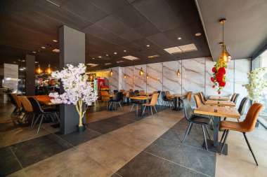 Modern ve zarif bir yemek alanı sunan güzel tasarlanmış bir restoran iç mekanı. Uzay, ahşap sandalyeler ve cam kaplamalı masalar da dahil olmak üzere çağdaş mobilyalara sahip..