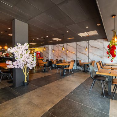 Modern ve zarif bir yemek alanı sunan güzel tasarlanmış bir restoran iç mekanı. Uzay, ahşap sandalyeler ve cam kaplamalı masalar da dahil olmak üzere çağdaş mobilyalara sahip..