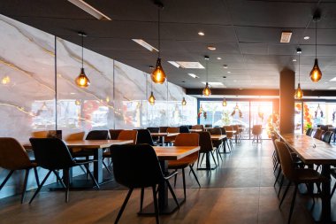 Konforlu ve modern kafe içi ahşap mobilyalar, sıcak ışıklandırma ve sokağa bakan büyük pencerelerle, davetkar bir atmosfer yaratıyor.