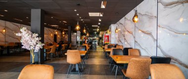 Modern ve zarif bir yemek alanı sunan güzel tasarlanmış bir restoran iç mekanı. Uzay, ahşap sandalyeler ve cam kaplamalı masalar da dahil olmak üzere çağdaş mobilyalara sahip..