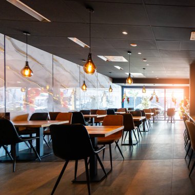 Konforlu ve modern kafe içi ahşap mobilyalar, sıcak ışıklandırma ve sokağa bakan büyük pencerelerle, davetkar bir atmosfer yaratıyor.