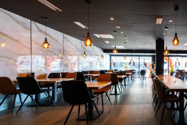 Konforlu ve modern kafe içi ahşap mobilyalar, sıcak ışıklandırma ve sokağa bakan büyük pencerelerle, davetkar bir atmosfer yaratıyor.