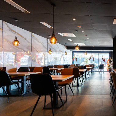 Konforlu ve modern kafe içi ahşap mobilyalar, sıcak ışıklandırma ve sokağa bakan büyük pencerelerle, davetkar bir atmosfer yaratıyor.