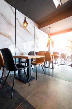 Konforlu ve modern kafe içi ahşap mobilyalar, sıcak ışıklandırma ve sokağa bakan büyük pencerelerle, davetkar bir atmosfer yaratıyor.