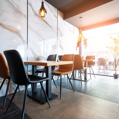 Konforlu ve modern kafe içi ahşap mobilyalar, sıcak ışıklandırma ve sokağa bakan büyük pencerelerle, davetkar bir atmosfer yaratıyor.