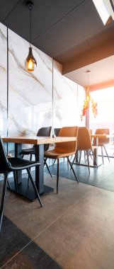 Konforlu ve modern kafe içi ahşap mobilyalar, sıcak ışıklandırma ve sokağa bakan büyük pencerelerle, davetkar bir atmosfer yaratıyor.