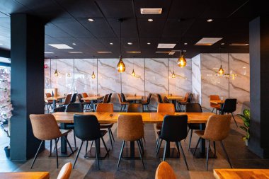 Konforlu ve modern kafe içi ahşap mobilyalar, sıcak ışıklandırma ve sokağa bakan büyük pencerelerle, davetkar bir atmosfer yaratıyor.