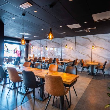 Konforlu ve modern kafe içi ahşap mobilyalar, sıcak ışıklandırma ve sokağa bakan büyük pencerelerle, davetkar bir atmosfer yaratıyor.