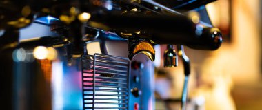 Otomatik kahve makinelerinin servis için hazır kahve bardağına akan yakın çekim görüntüsü. Kahve aroması tüm dükkânı ve sıcak görünen atölye atmosferini kaplıyor.