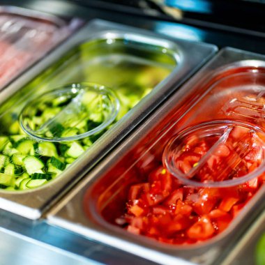 Profesyonel mutfak ortamında çeşitli sebze ve malzemelerle dolu metal kaplar, dikey görüntü.