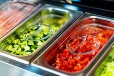 Profesyonel mutfak ortamında çeşitli sebze ve malzemelerle dolu metal kaplar, dikey görüntü.