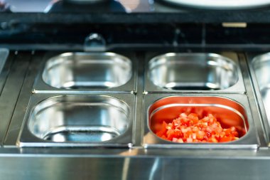 Profesyonel mutfak ortamında çeşitli sebze ve malzemelerle dolu metal kaplar, dikey görüntü.