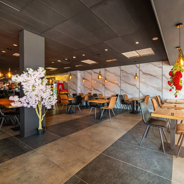 Modern ve zarif bir yemek alanı sunan güzel tasarlanmış bir restoran iç mekanı. Uzay, ahşap sandalyeler ve cam kaplamalı masalar da dahil olmak üzere çağdaş mobilyalara sahip..