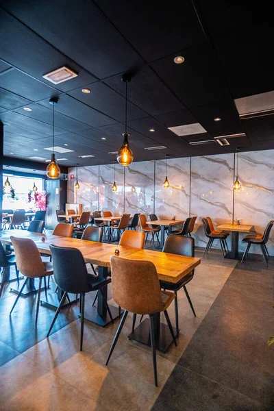 Konforlu ve modern kafe içi ahşap mobilyalar, sıcak ışıklandırma ve sokağa bakan büyük pencerelerle, davetkar bir atmosfer yaratıyor.