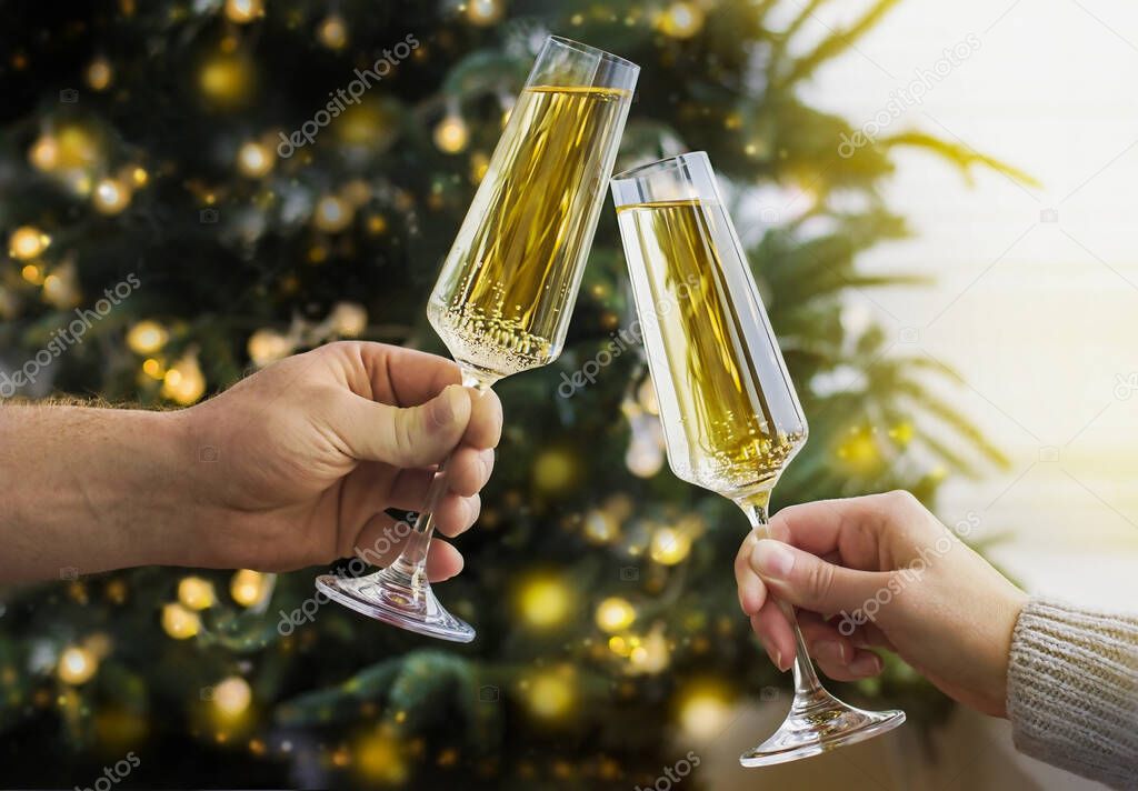 man and woman clink glasses of champagne against the background of a christmas tree