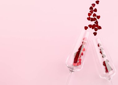 İki şarap kadehi ve konfeti pembe arka planda kalp şeklinde dağılmış.