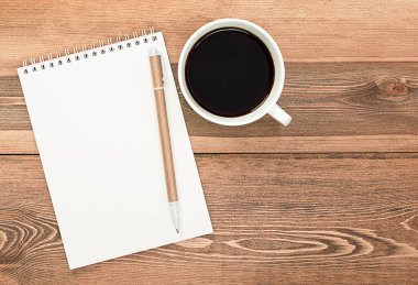 Ahşap çalışma masasının üzerinde kalem ve kahve fincanı olan defter.