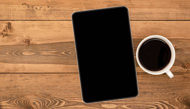 Tablet bilgisayar ve kahve fincanı ahşap masada.