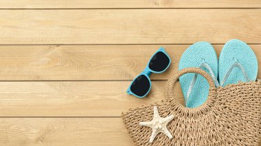 Güneş gözlüklü plaj çantası ve tahta arka planda parmak arası terlikler.