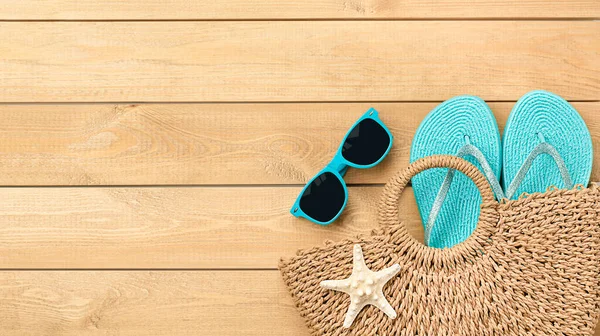 Güneş gözlüklü plaj çantası ve tahta arka planda parmak arası terlikler.