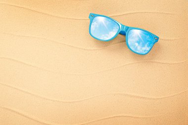 Gökyüzünün yansıması olan bir güneş gözlüğü deniz kumunda yatıyor.