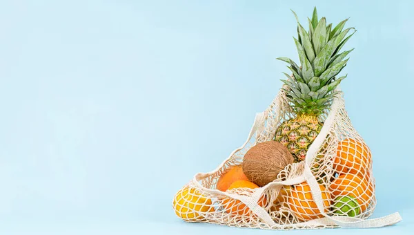 mesh bag with tropical fruits on light blue background