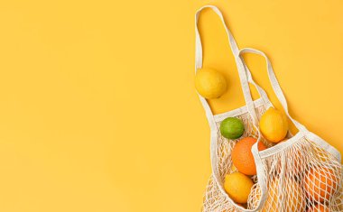 Taze portakallar, limonlar, limonlar ve greyfurt sarı arka planda bir ağ torbasında.