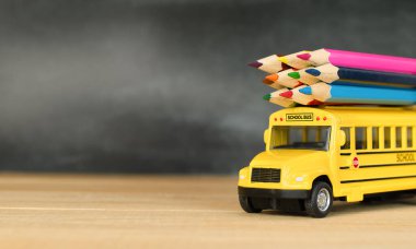 Oyuncak okul otobüsü. Sınıftaki ahşap masada renkli kalemler.